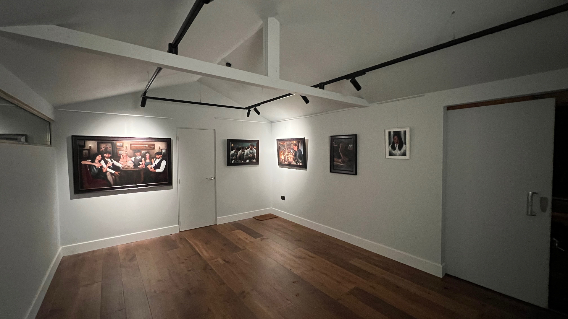 The gallery seen from the opposite corner, the architecture quiet and each painting holding its own pool of light.