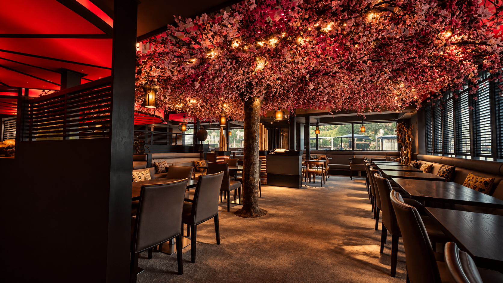 Wide view of the dining room bathed in red ceiling light, an illuminated cherry-blossom canopy above dark timber tables.